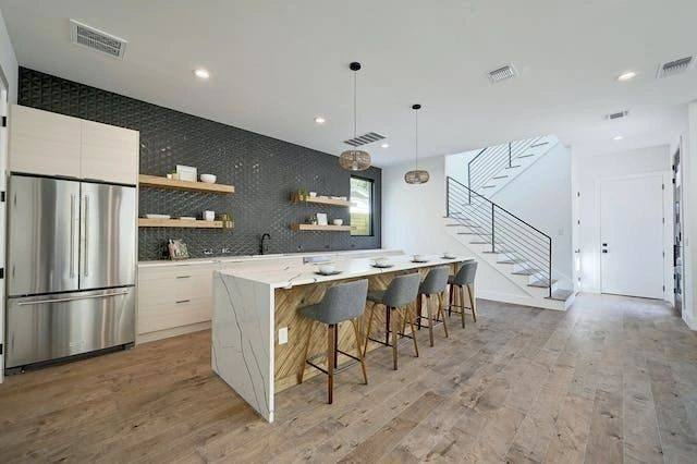 Kitchen island with open shelving, dark tile wall and floating stair beyond