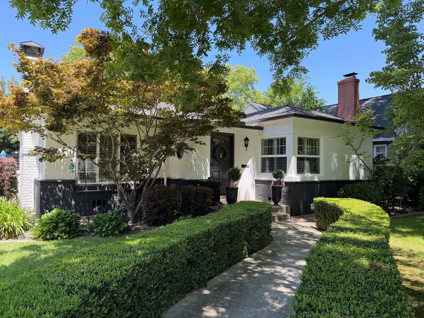 Repainted single-story cottage with pale stucco, black painted brick base and manicured boxwood hedges in Sacramento