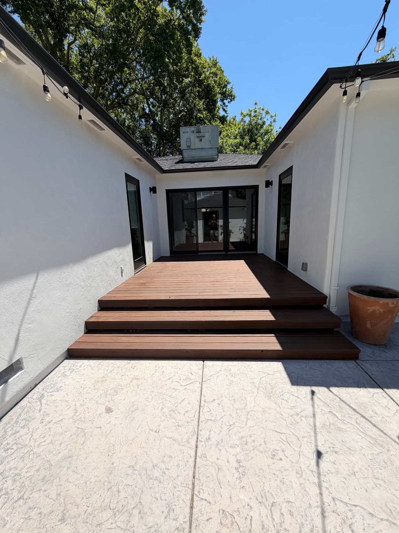 White stucco courtyard with a stained hardwood deck, stamped concrete patio and black framed sliding doors