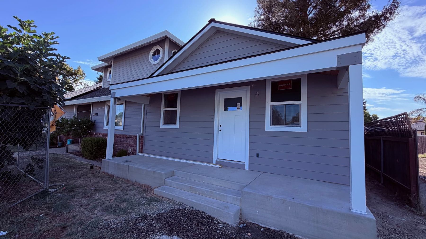 Craftsman home addition in gray lap siding with a new covered front porch, white trim and poured concrete steps