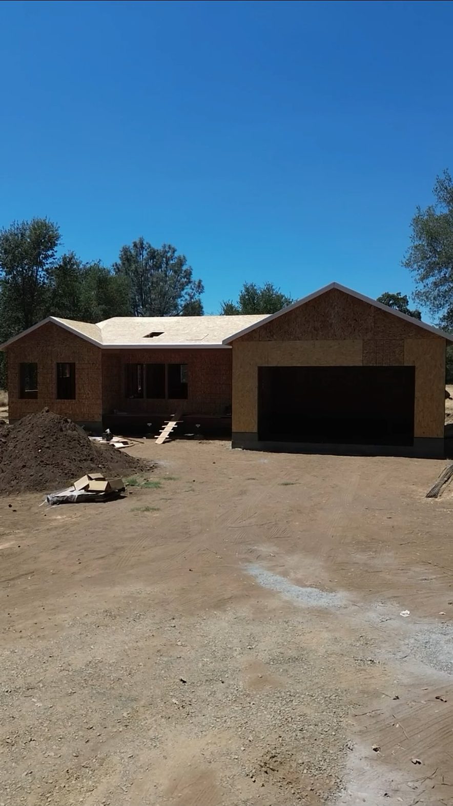 Framed and sheathed single-story custom home shell with the garage opening cut on a foothill lot