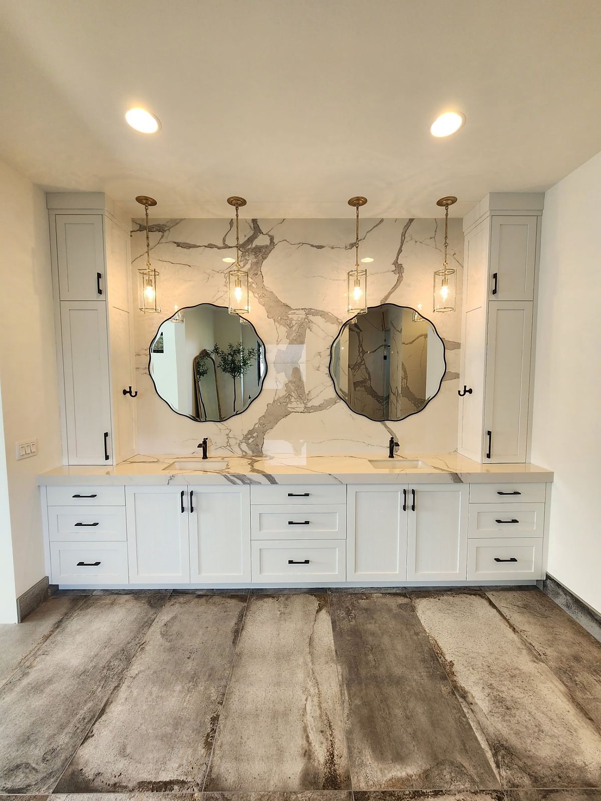 Double vanity with book-matched marble slab wall, scalloped mirrors and brass pendants