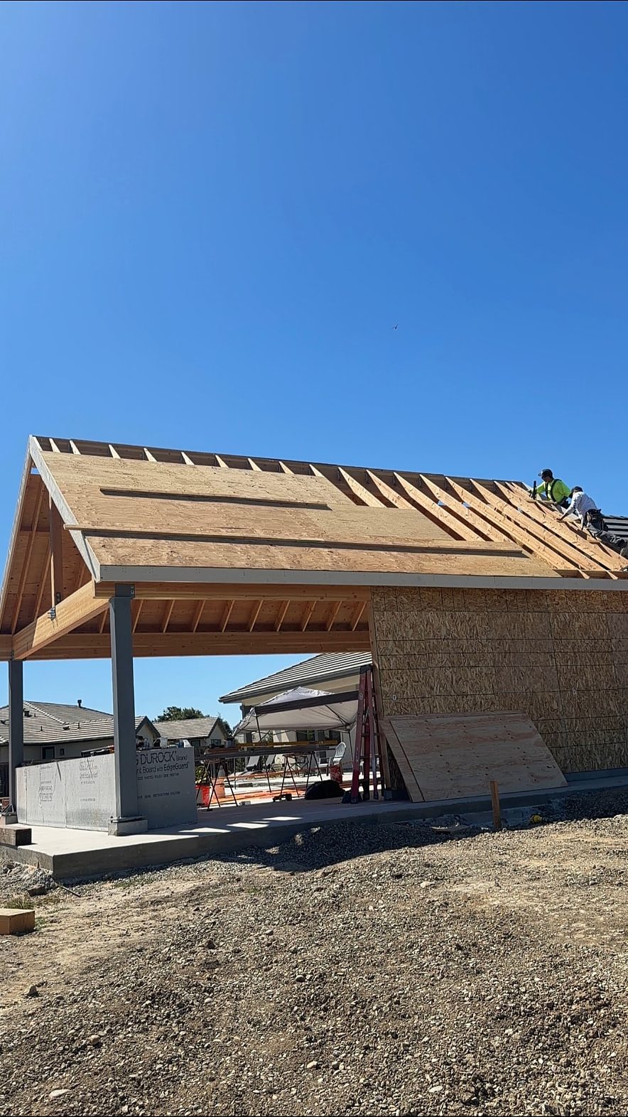 Timber gable and rafters sheathed over a covered outdoor room while roofers work the main roof