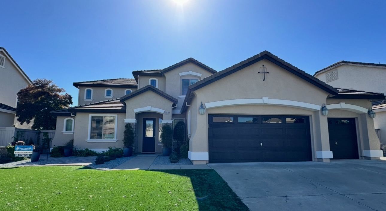 Two-story stucco home with freshly painted trim and dark garage doors after a Lane Built exterior repaint